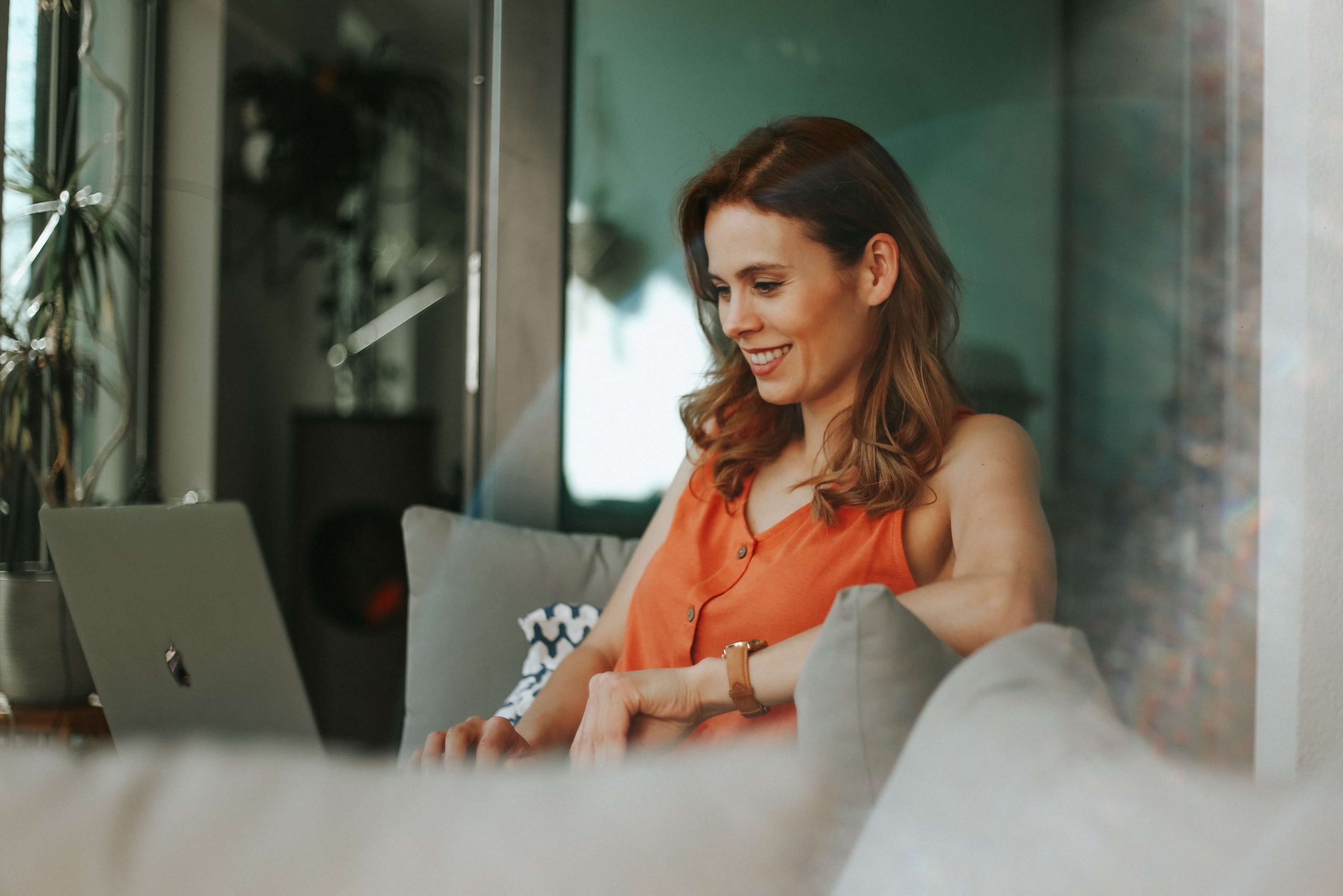 woman sitting on a sofa with her laptop smiling