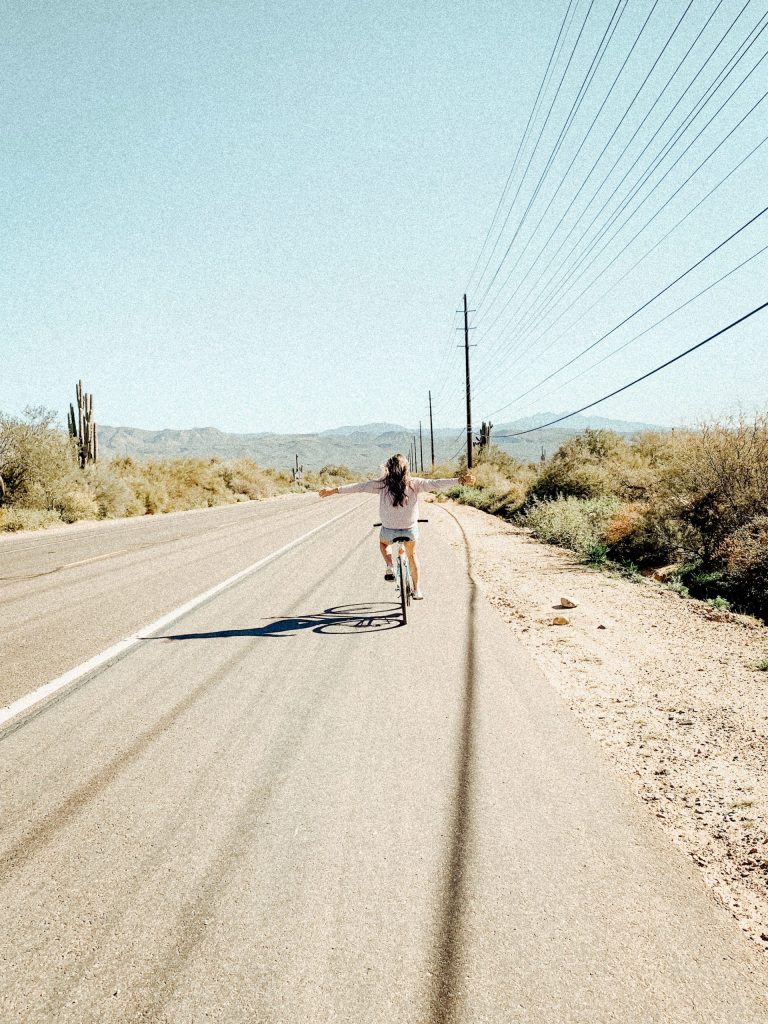 woman riding bike on dirt road stretching out her arms